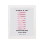 Bible wall art displaying The Fruit of the Spirit verse from Galatians 5:22-23 with pink brushstrokes on a white background. hung on the wall in a white frame