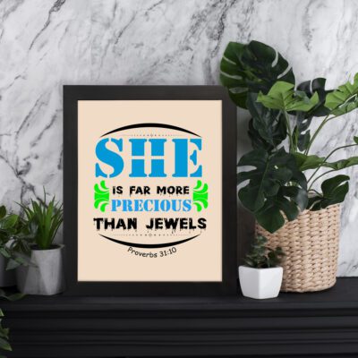 She Is Far More Precious Than Jewels Proverbs 31:10 Bible verse wall art with bold blue text and green ornamental frame, beige background. displayed on the table in a black frame