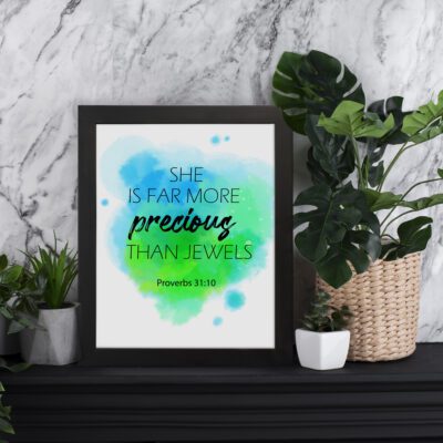 She Is Far More Precious Than Jewels Proverbs 31:10 Bible Wall Art with watercolor design in blue and green displayed on the table in a black frame