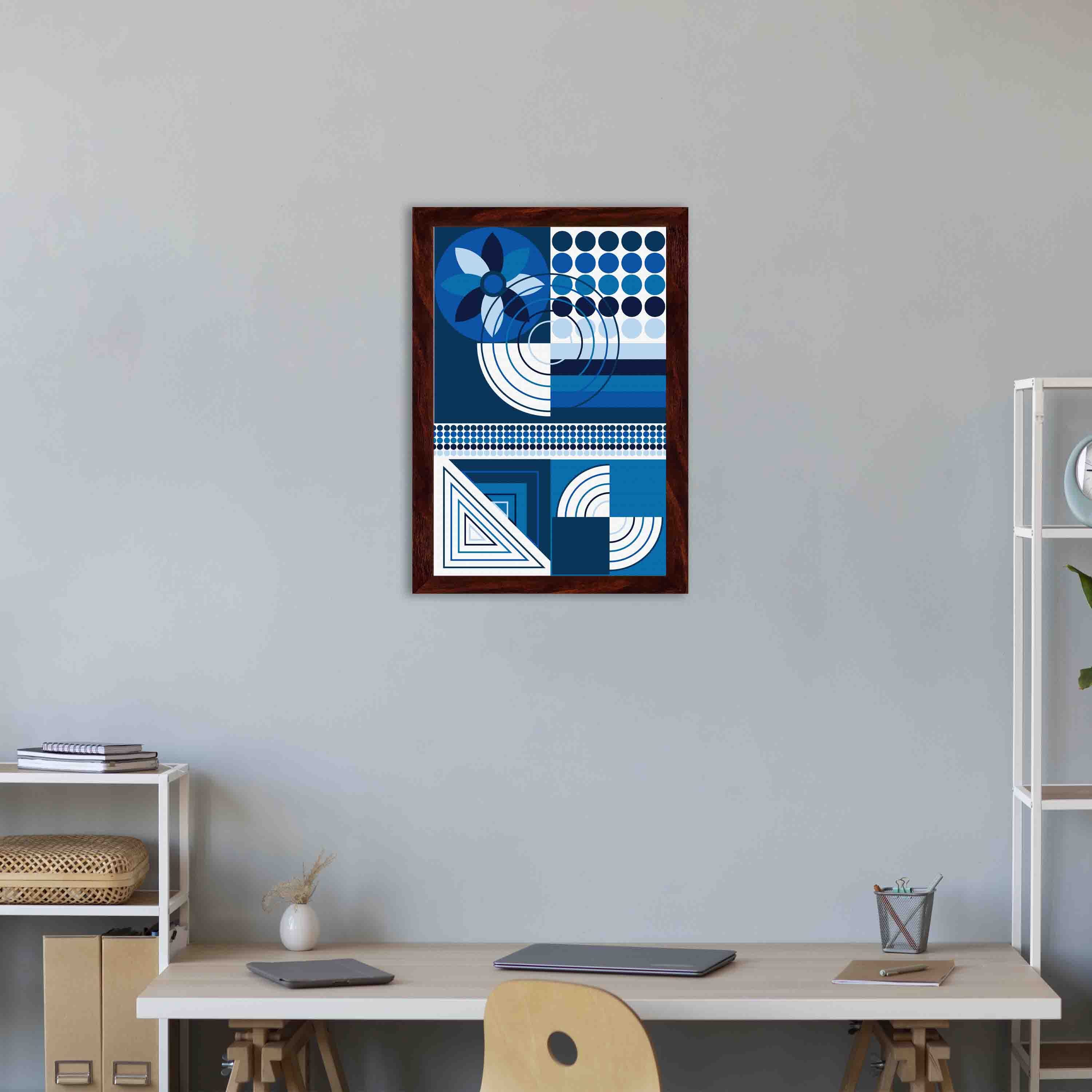Abstract wall art with geometric shapes in blue, white, and black, framed in black, displayed on a light gray wall in a cozy setting.