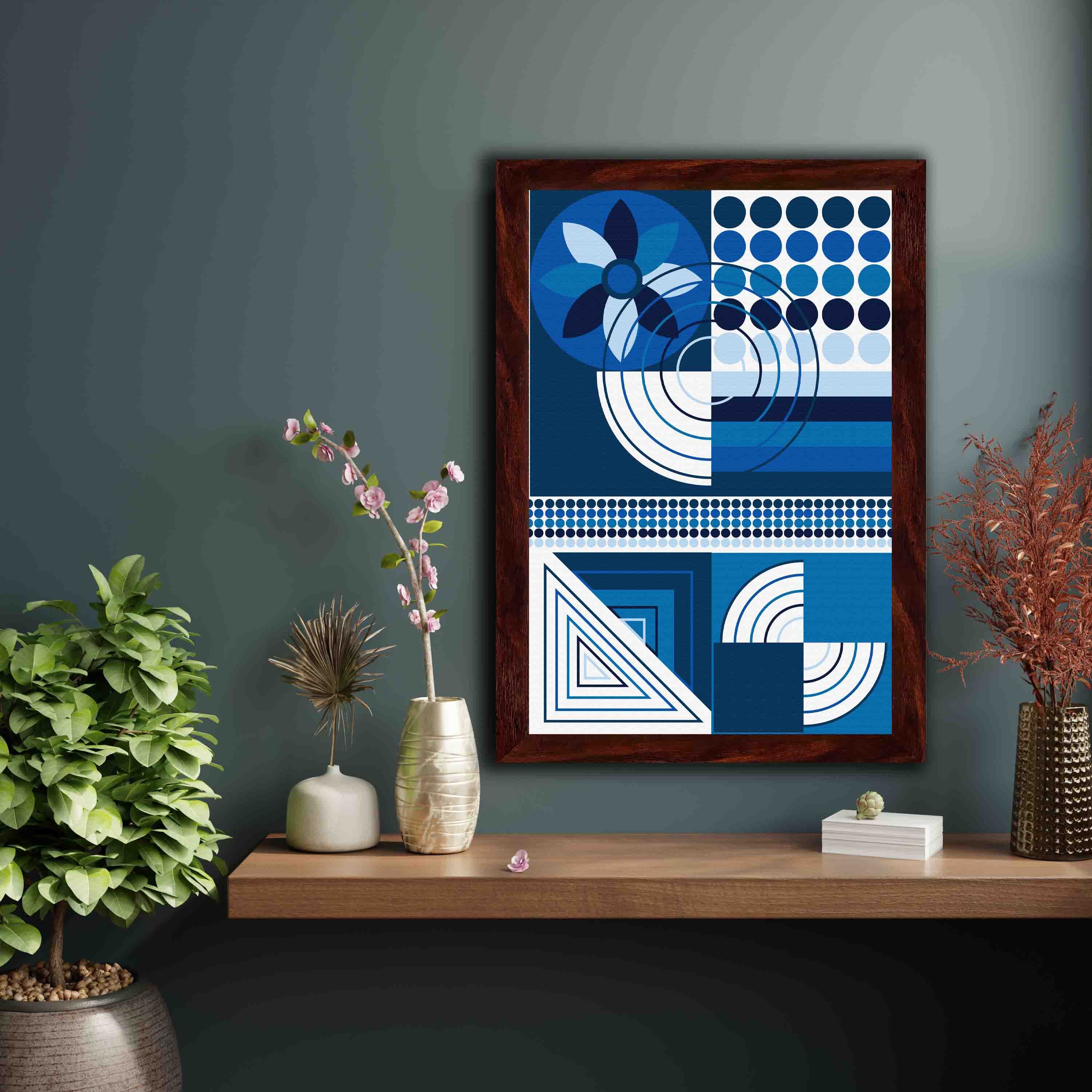 Abstract wall art with geometric shapes in blue, white, and black, framed in black, displayed on a light gray wall in a cozy setting.