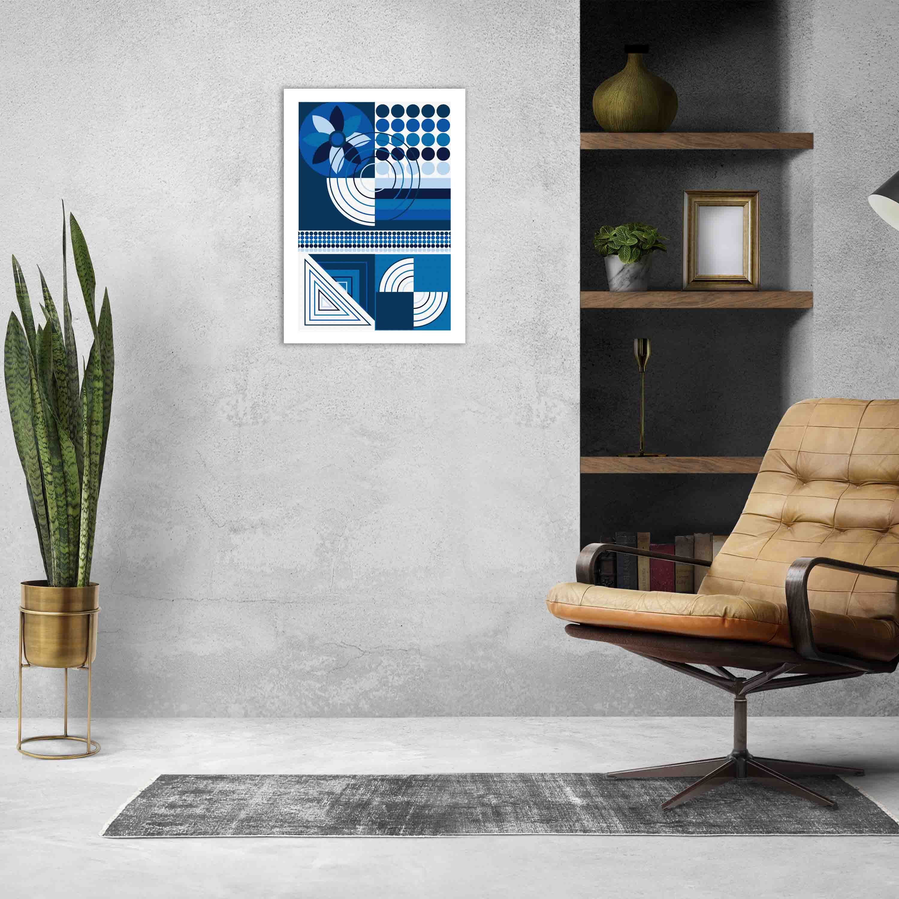 Abstract wall art with geometric shapes in blue, white, and black, framed in black, displayed on a light gray wall in a cozy setting.