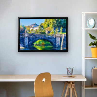 Scenic wall art of a stone bridge over a calm river, surrounded by green trees and a blue sky, set against a light gray or off-white wall.