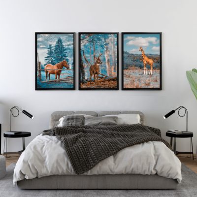 Set of three art prints featuring a horse, deer, and giraffe in nature, with shades of blue, brown, and orange, framed in black. displayed on the wall in a black frame