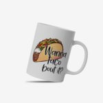 White coffee mug with a colorful taco illustration and the phrase "Wanna taco 'bout it?" in a playful, handwritten-style black font. Microwave-friendly espresso cup.