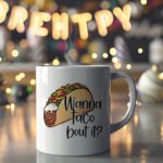 White coffee mug with a colorful taco illustration and the phrase "Wanna taco 'bout it?" in a playful, handwritten-style black font. Microwave-friendly espresso cup.