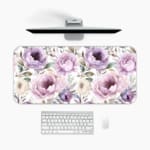 Infidu Flowers Design Desk Pad with green leaves and large purple and pink flowers on a light, neutral background. A desk pad under the computer