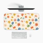 Infidu Colorful Floral Design Desk Pad with vibrant flowers in yellow, pink, blue, orange, and green on a light pink background. A desk pad under the computer