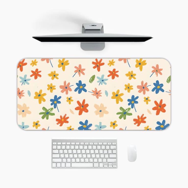 Infidu Colorful Floral Design Desk Pad with vibrant flowers in yellow, pink, blue, orange, and green on a light pink background. A desk pad under the computer