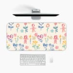 Desk pad with childlike drawings of flowers, stick figures, and hearts in pastel blue, pink, and yellow. A desk pad under the computer