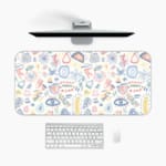 Desk pad with whimsical symbols including eyes, geometric shapes, and abstract designs in light blue, pink, and orange. A desk pad under the computer