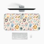 Infidu desk pad with soft pastel floral design on a light pink background, featuring delicate light blue, pink, and beige flowers. A desk pad under the computer