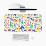 Bright desk mat featuring colorful animals, plants, and abstract shapes on a white background. A desk pad under the computer