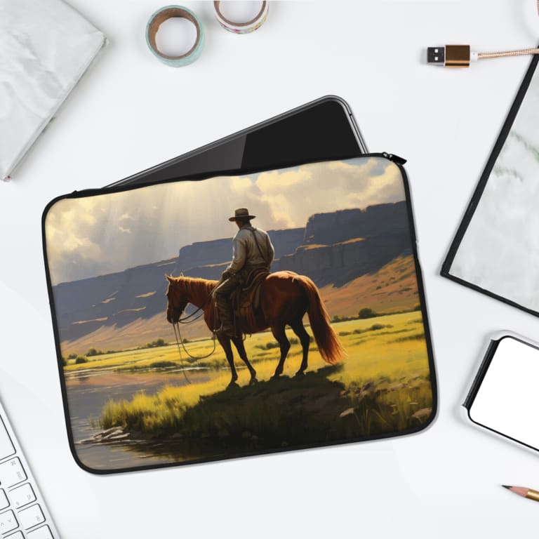 Cowboy River Laptop Sleeve featuring a scenic Western design with a cowboy on horseback near a river, green grass, and mountains. laptop sleeve kept on a plain white background