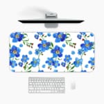 Desk pad with blue flowers, yellow centers, and green leaves on a white background. A desk pad under the computer