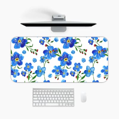 Desk pad with blue flowers, yellow centers, and green leaves on a white background. A desk pad under the computer