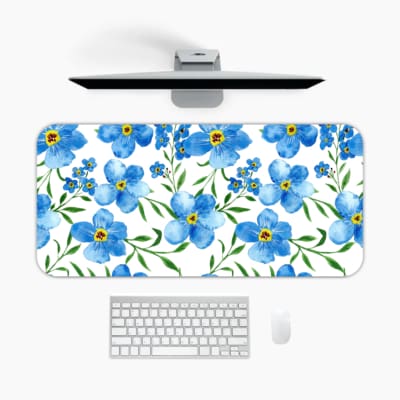 Desk pad with light blue flowers, yellow centers, and green leaves on a white background. A desk pad under the computer