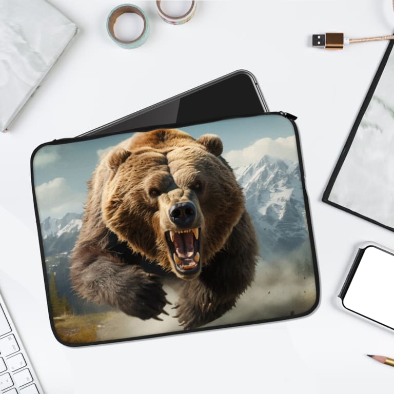 Laptop sleeve featuring a roaring brown bear with a rugged, snowy mountain background, made with durable fabric and a secure zip closure. laptop sleeve kept on a plain white background