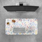 Desk pad with whimsical symbols including eyes, geometric shapes, and abstract designs in light blue, pink, and orange. Desk Pad with Keyboard and Mouse on top of the desk pad