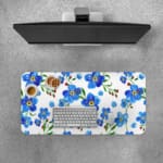 Desk pad with blue flowers, yellow centers, and green leaves on a white background. Desk Pad with Keyboard and Mouse on top of the desk pad