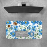 Desk pad with light blue flowers, yellow centers, and green leaves on a white background. Desk Pad with Keyboard and Mouse on top of the desk pad