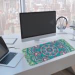 Infidu Colorful Teal and Pink Mandala Design Desk Pad with intricate teal, pink, and white patterns. A computer and laptop are next to the desk pad