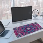 Infidu Colorful Mandala Desk Pad featuring a vivid mandala pattern with symmetrical shapes in pink, purple, and blue tones. A computer and laptop are next to the desk pad