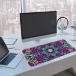 Infidu Colorful Mandala Design Desk Pad with intricate blue, pink, and purple patterns on a light background. A computer and laptop are next to the desk pad