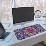 Infidu Colorful Geometric Pattern Desk Pad with pink, blue, yellow, and black geometric shapes on a soft yellow background. A computer and laptop are next to the desk pad
