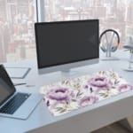 Infidu Soft Floral Desk Pad with white background, large purple and lavender flowers, and light gray and blue leaves. A computer and laptop are next to the desk pad