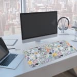 Infidu desk pad with pastel abstract shapes and symbols on a pale blue background. A computer and laptop are next to the desk pad
