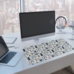 Blue abstract patterns including geometric shapes and faces on a white desk pad. A computer and laptop are next to the desk pad