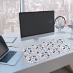 Desk pad with playful blue and dark blue bear patterns on a white background. A computer and laptop are next to the desk pad