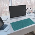 Desk pad with a green background and white ripple design, resembling water-like waves. A computer and laptop are next to the desk pad