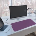 Desk pad with a purple textured background and black diamond design. A computer and laptop are next to the desk pad