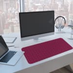 Pink desk pad with a pattern of small dots. A computer and laptop are next to the desk pad
