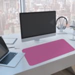 Pink desk pad with a pattern of small dots. A computer and laptop are next to the desk pad
