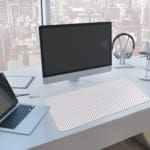 Desk pad with a white background and light gray diagonal stripes. A computer and laptop are next to the desk pad