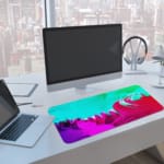 Infidu Vibrant Green and Pink Gradient Desk Pad with wave-like patterns in green, pink, and purple A computer and laptop are next to the desk pad