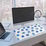 Desk pad with blue flowers evenly spaced on a white background. A computer and laptop are next to the desk pad