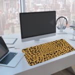Infidu Leopard Print Desk Pad features a leopard print pattern with a tan background and black spots, resembling natural leopard fur. A computer and laptop are next to the desk pad