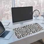 Infidu Bold Black and White Abstract Print Desk Pad with black abstract shapes on a white background, resembling animal print. A computer and laptop are next to the desk pad
