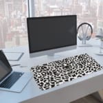 Infidu White Desk Pad with black spotted leopard print design on a white background, adding a chic touch. A computer and laptop are next to the desk pad