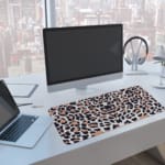 Infidu White Desk Pad with Bold Leopard Print Design featuring black and brown spots on a white background. A computer and laptop are next to the desk pad