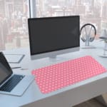 Light pink and white polka dot desk pad with a classic pattern design. A computer and laptop are next to the desk pad