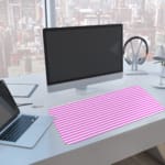 Pink and white striped desk pad with horizontal lines on a white background. A computer and laptop are next to the desk pad