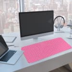 Pink desk pad with a pattern of small, evenly spaced triangles. A computer and laptop are next to the desk pad