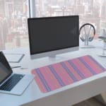 Infidu desk pad with a pink background and vertical columns of blue and yellow dots. A computer and laptop are next to the desk pad