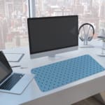 Desk pad featuring small black polka dots on a blue background. A computer and laptop are next to the desk pad