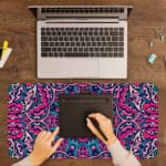 Infidu Colorful Mandala Desk Pad featuring a vivid mandala pattern with symmetrical shapes in pink, purple, and blue tones. A writing pad on top of the desk pad